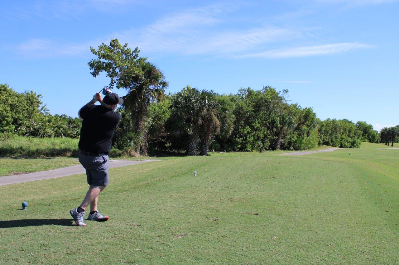A man is seen from behind, mid-golf-swing