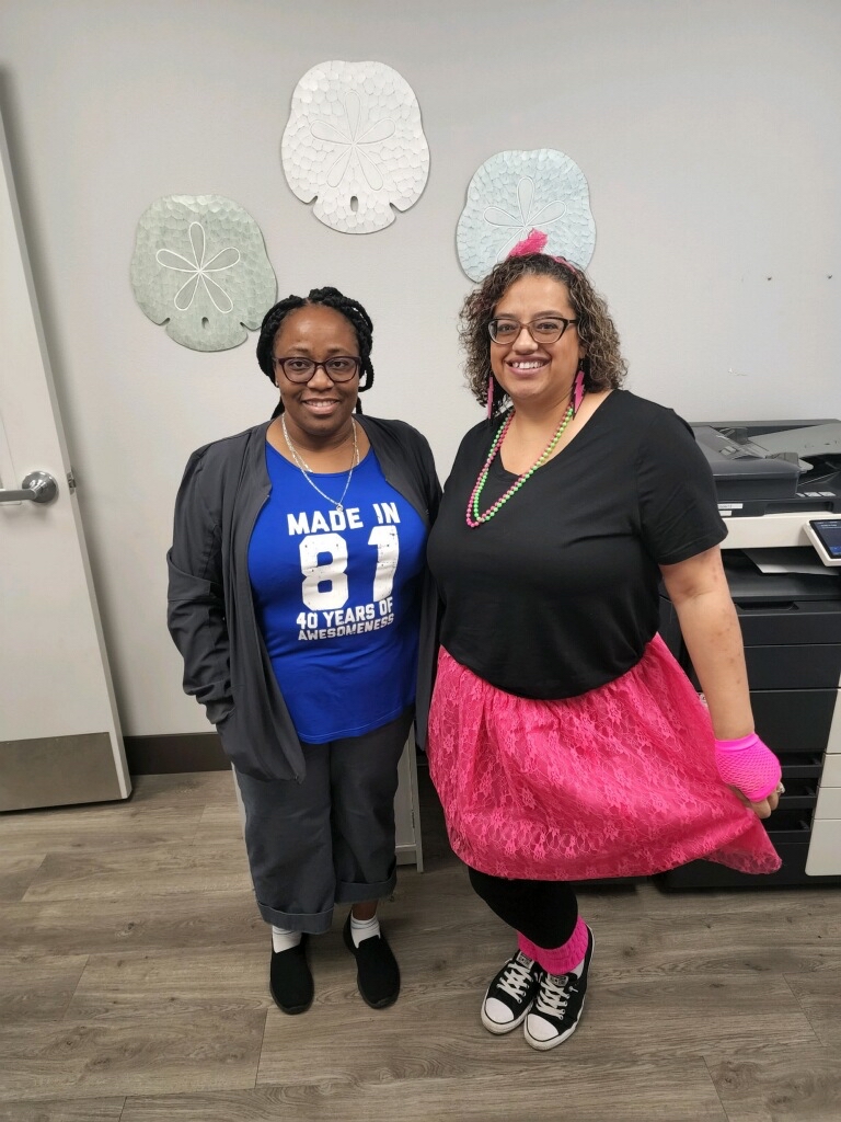 Two Florida Pain Staff in 80s clothes smiling at the camera, one holding their pink tutu